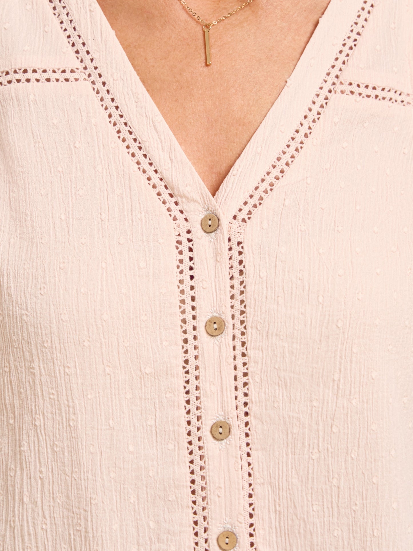 Close-up of a light pink blouse with button details and embroidery.