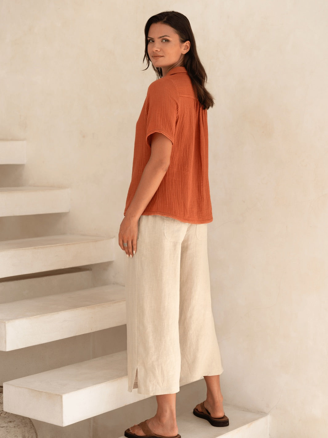 Woman in an orange top and white pants standing on a staircase.