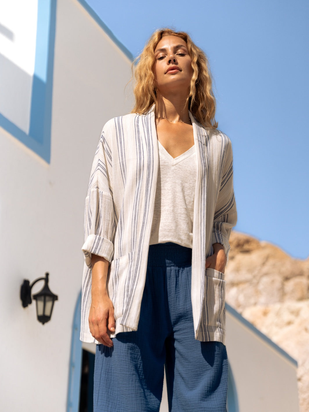Woman wearing a striped jacket and blue pants standing outdoors with a clear sky.