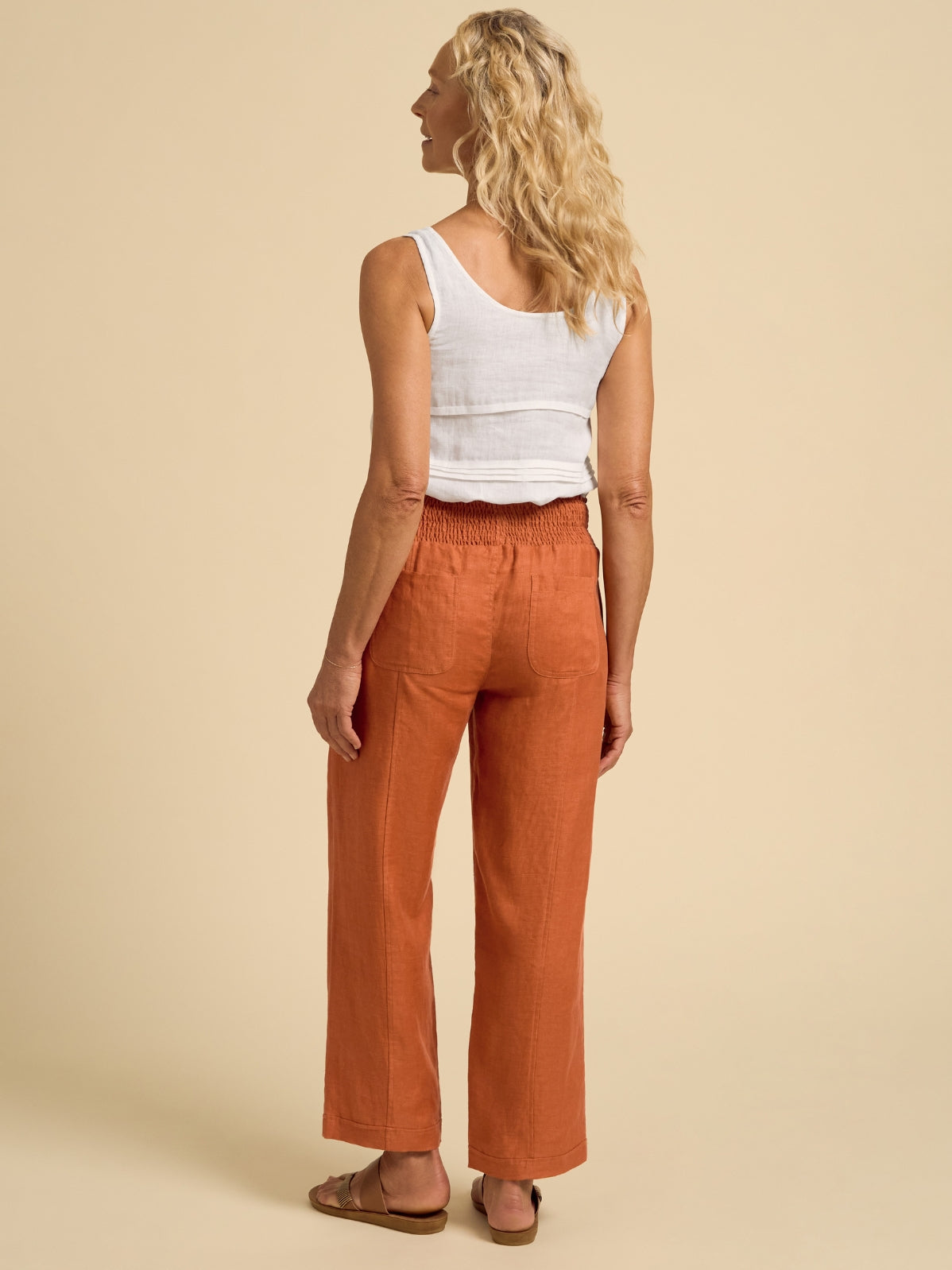 Woman wearing orange pants and a white top on a beige background