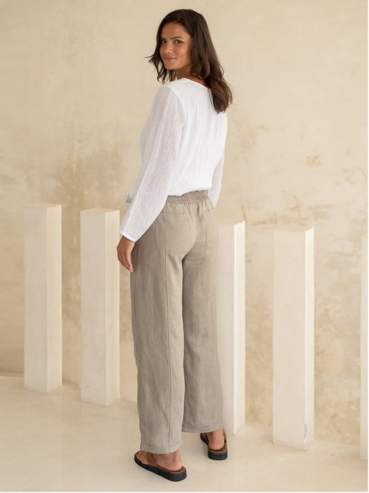 Woman wearing a white blouse and beige pants standing against a neutral background