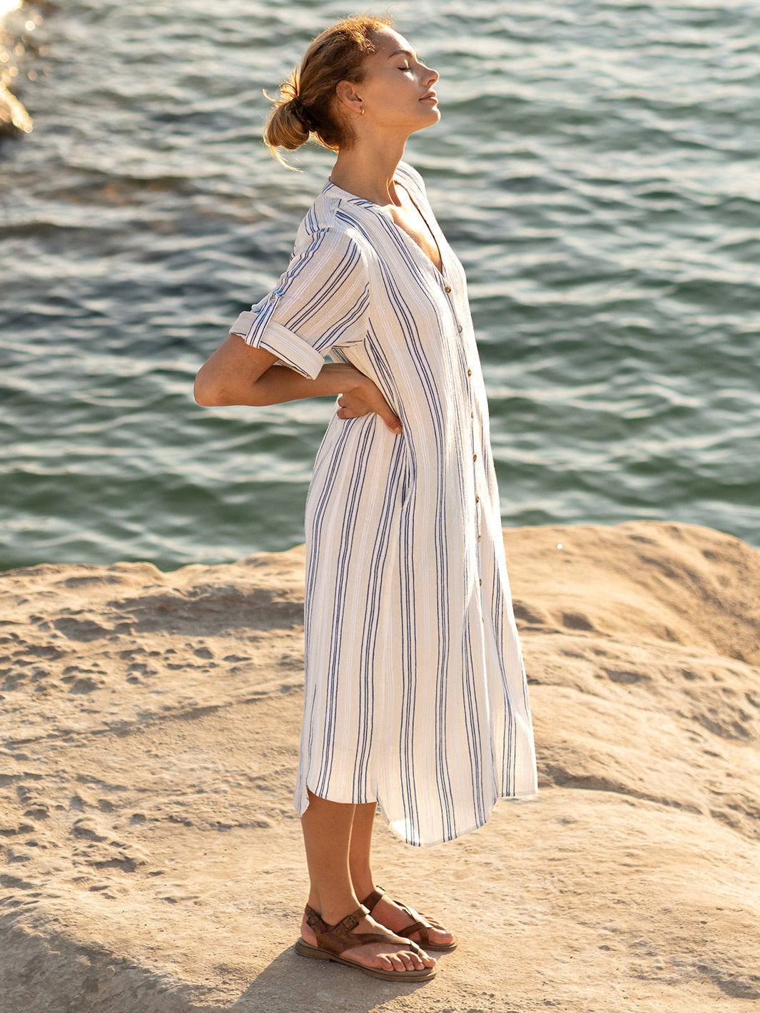Woman in a striped dress standing on a rocky shore with water in the background