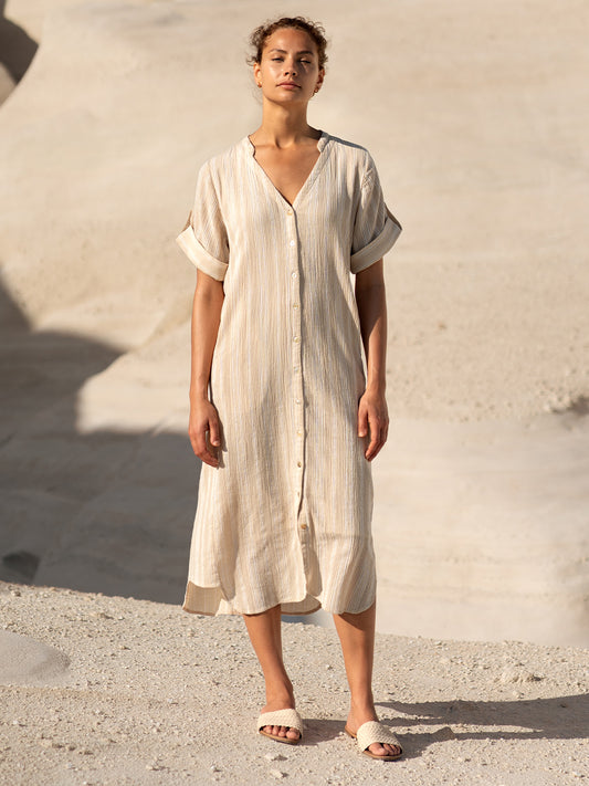 Woman wearing a beige dress standing against a textured wall.