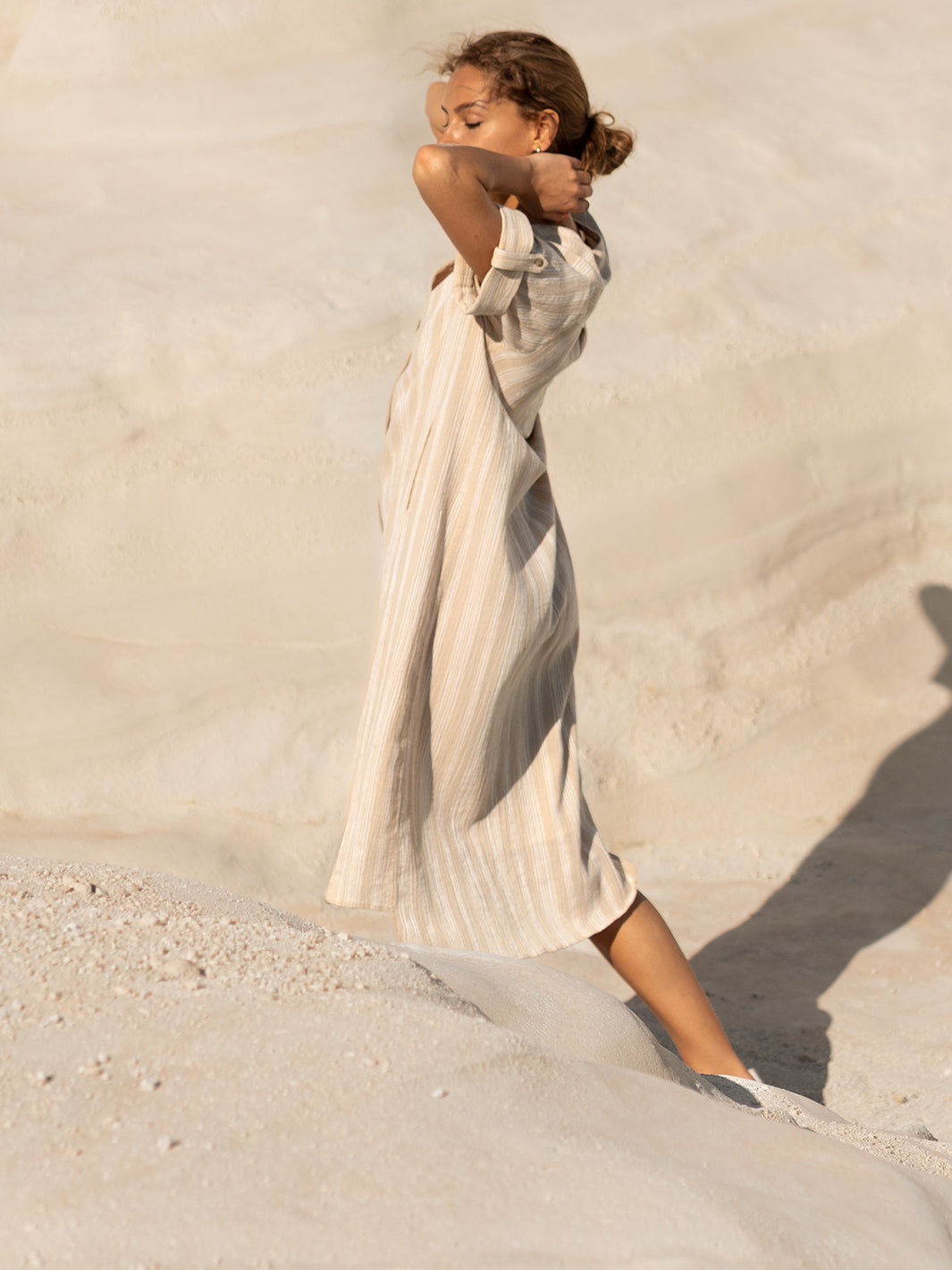 Woman in a long, light-colored dress standing on sand with a neutral background
