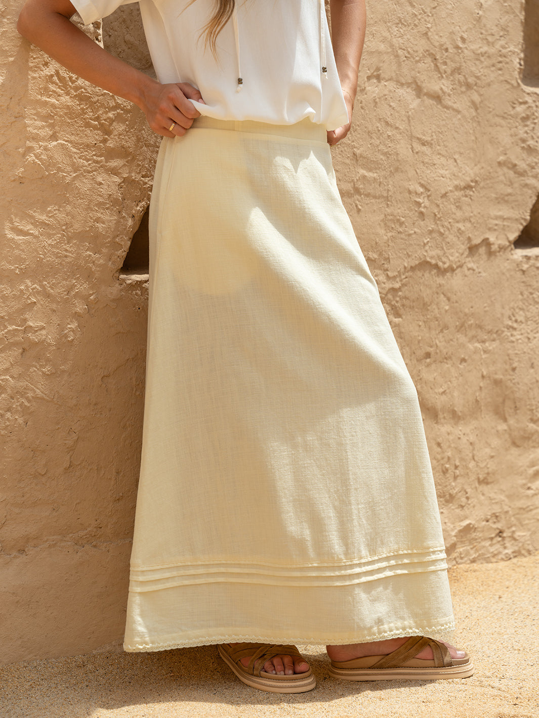 Person wearing a long, light-colored skirt against a beige wall.