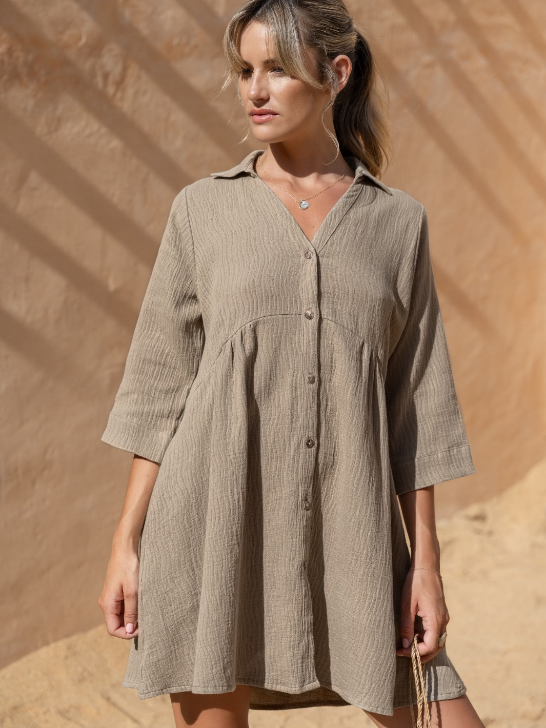 Woman wearing a beige button-up dress against a sandy background