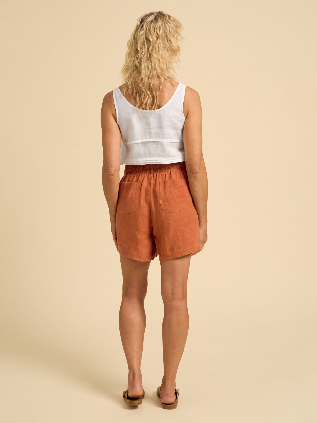 Woman wearing a white tank top and rust-colored shorts on a beige background
