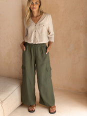 Woman wearing a beige shirt and green cargo pants against a beige wall.