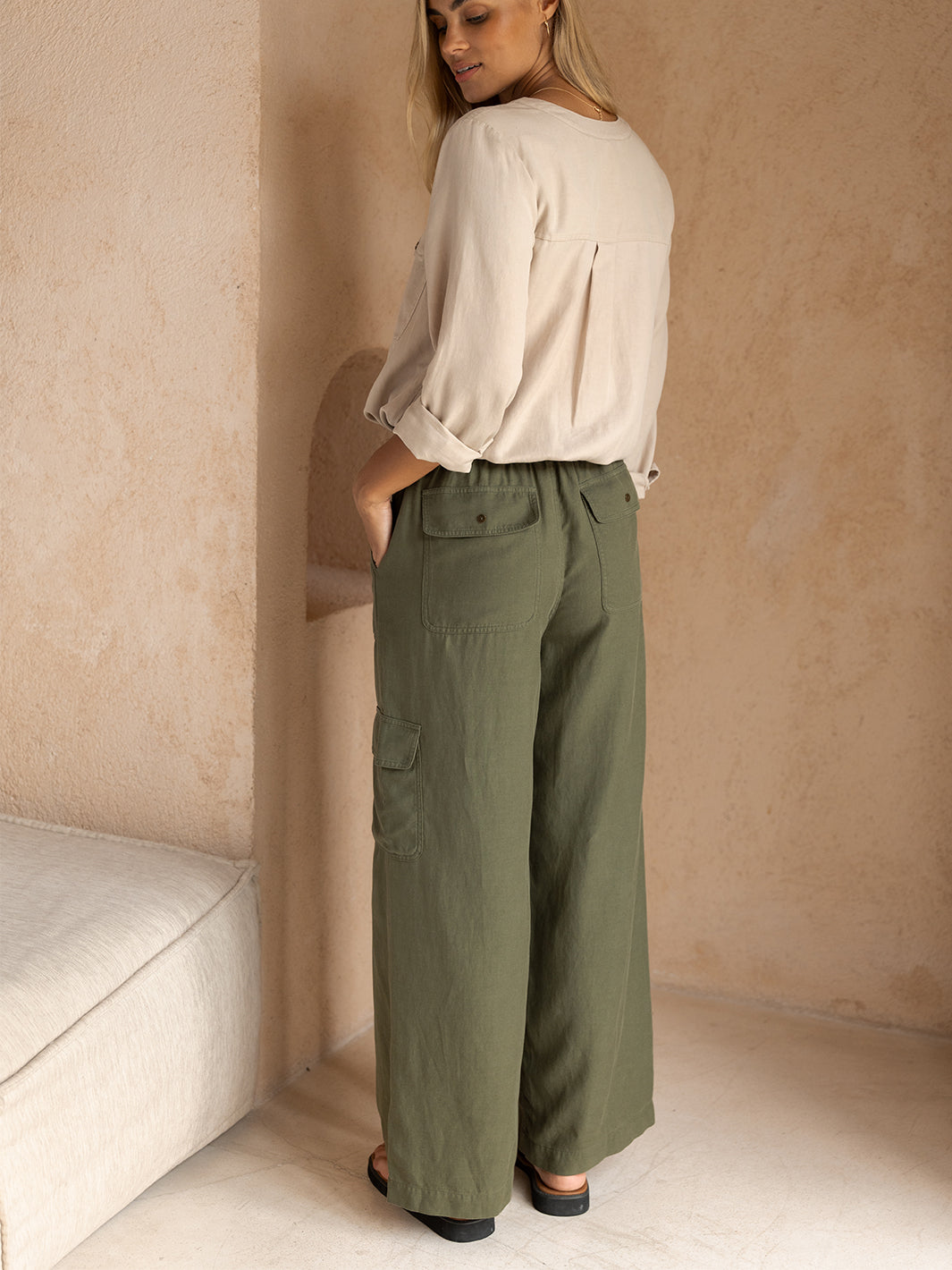 Woman wearing a beige blouse and green cargo pants against a beige wall.