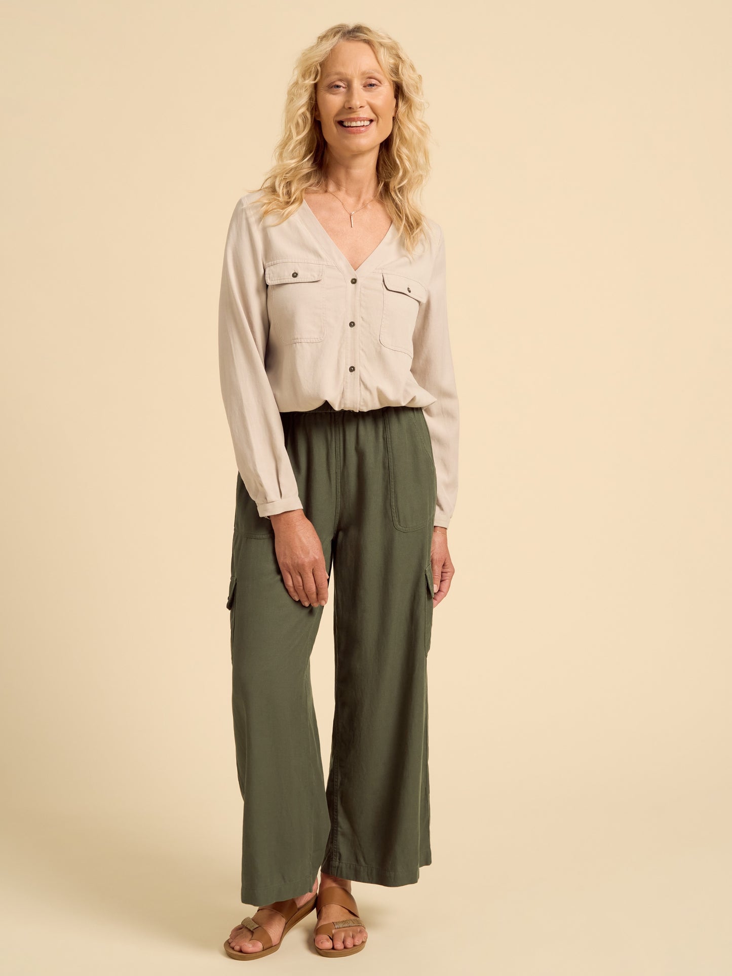 Woman wearing a light-colored blouse and green pants on a beige background