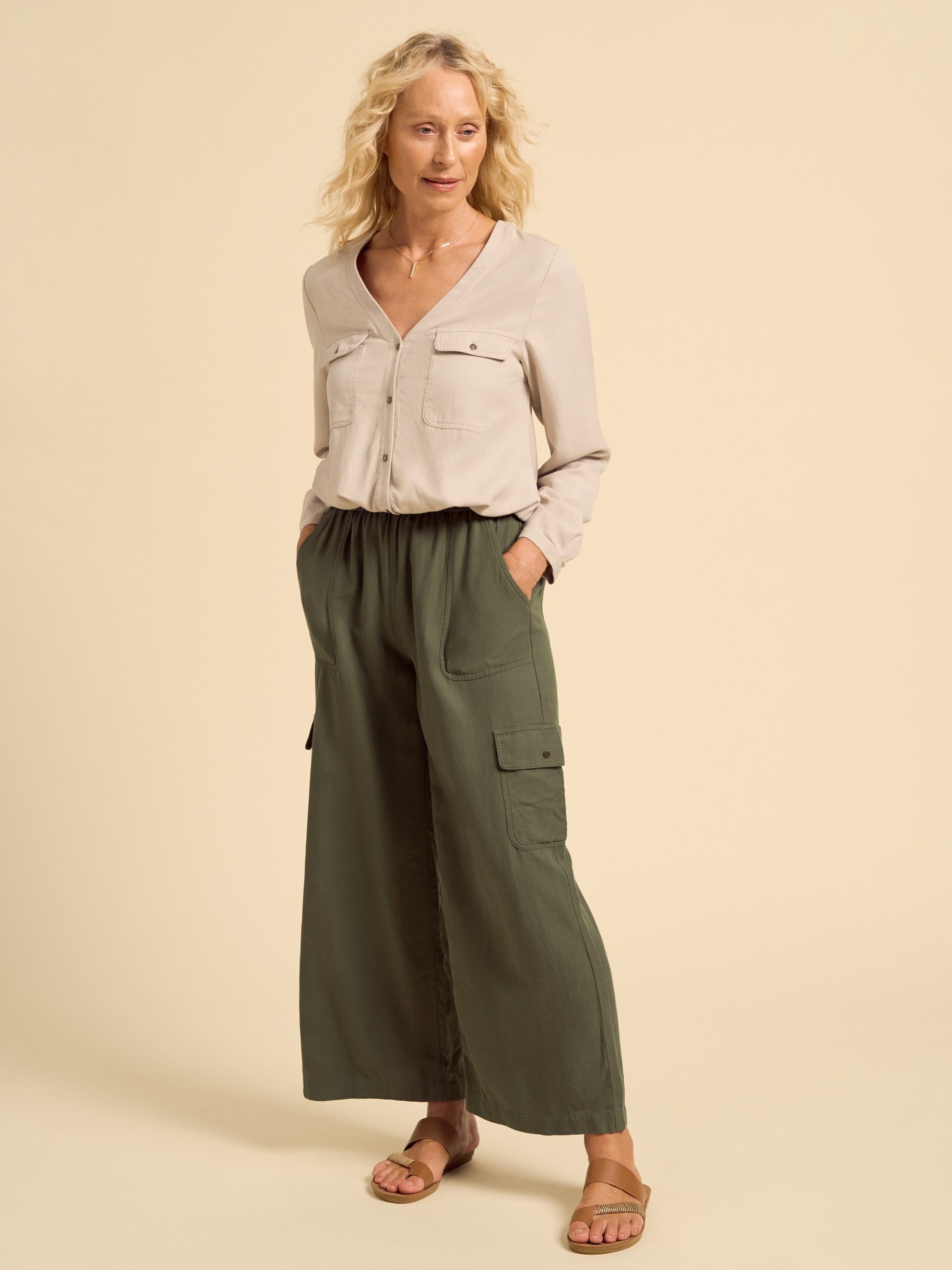 Woman wearing a beige shirt and green cargo pants on a beige background