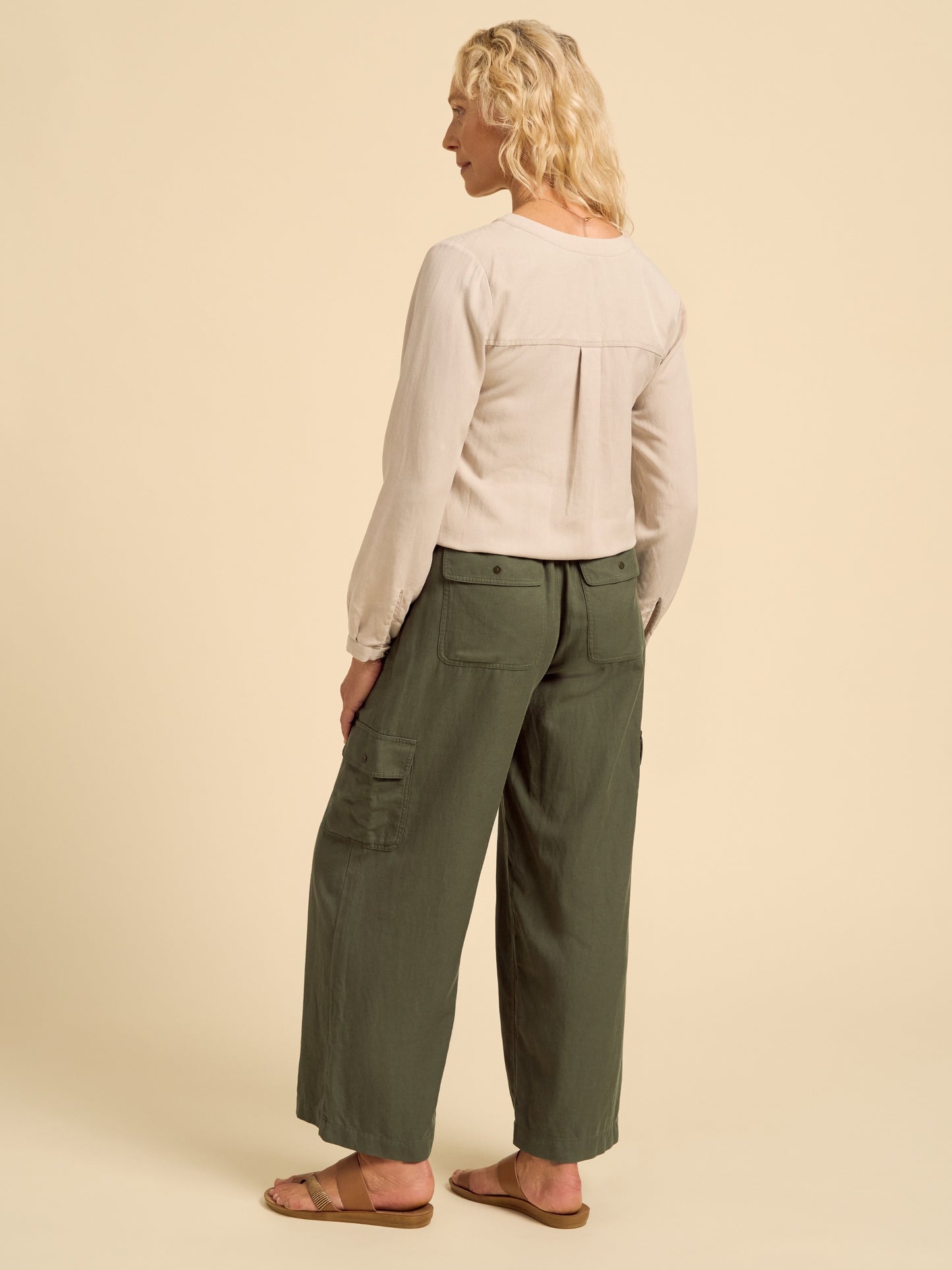 Woman wearing a beige long-sleeve top and green cargo pants on a beige background