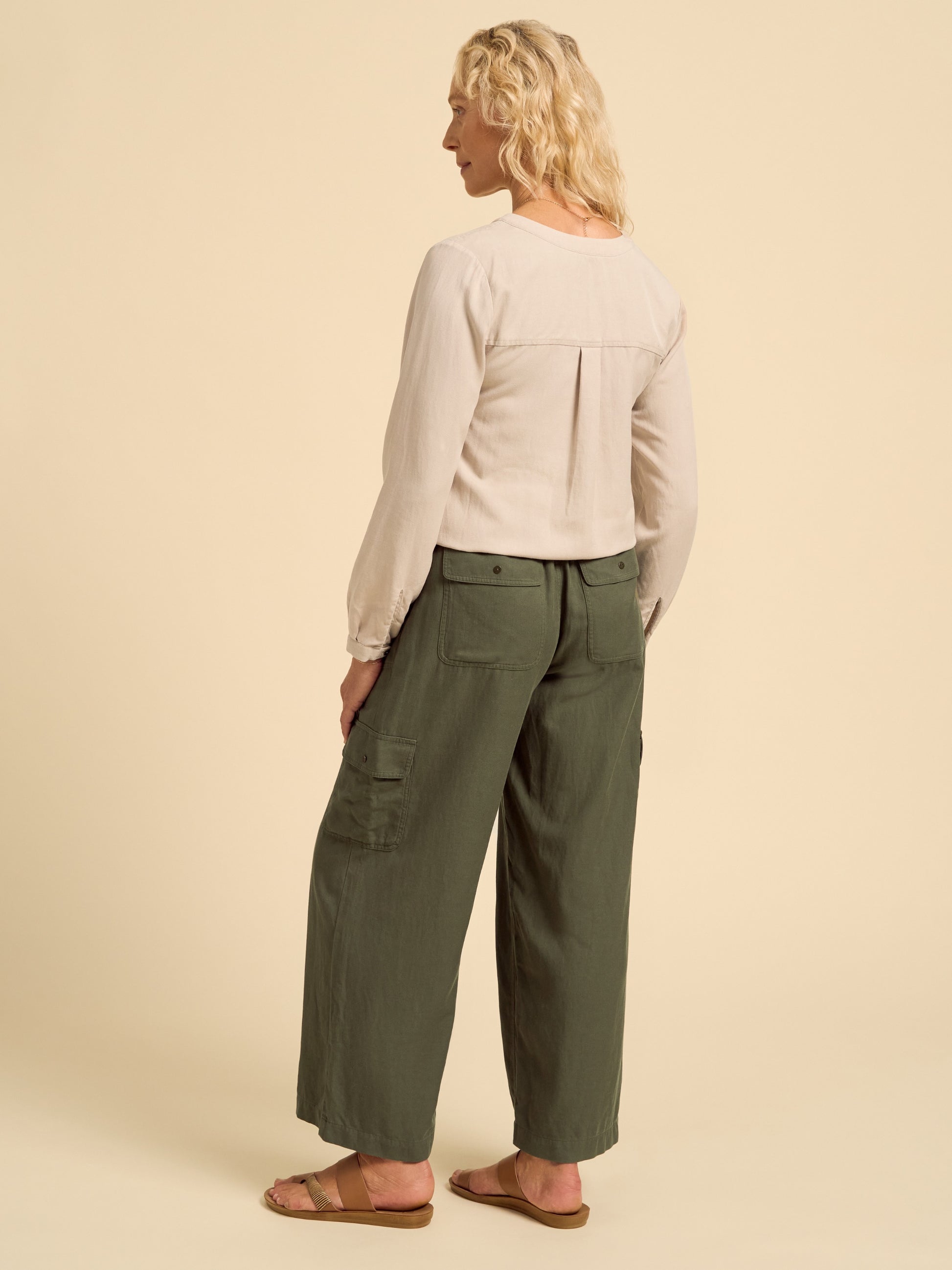 Woman wearing a beige long-sleeve top and green cargo pants on a beige background