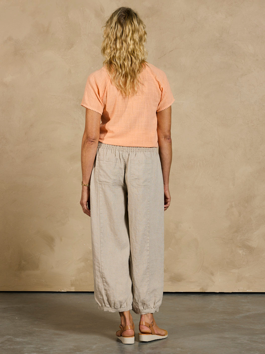 Person wearing a peach t-shirt and beige pants against a beige wall.