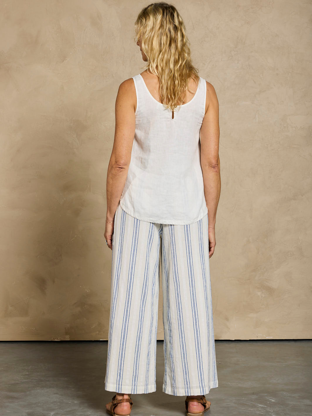 Woman wearing a white sleeveless top and striped pants against a beige wall.