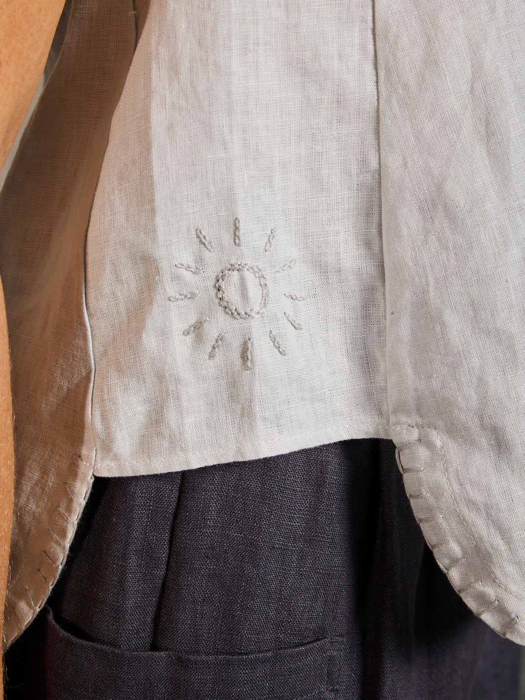 Close-up of a garment with embroidered sun design on a plain background