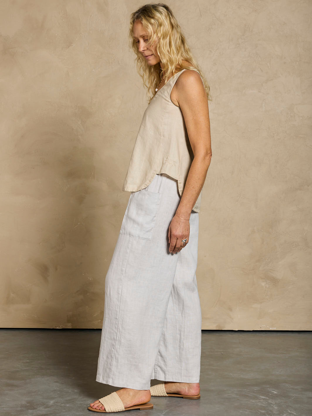 Woman wearing a beige sleeveless top and light-colored pants against a plain background