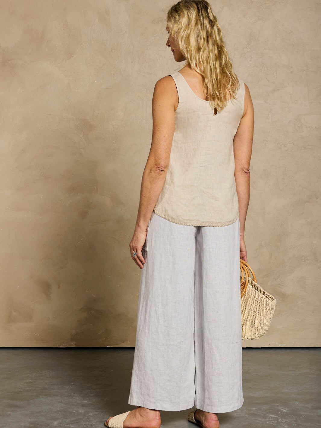 Woman wearing a beige sleeveless top and light gray wide-leg pants against a beige wall.