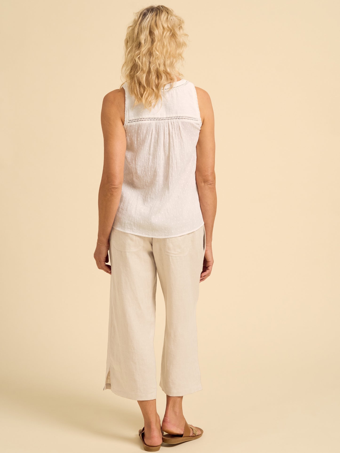 Woman wearing a white sleeveless top and beige pants on a beige background