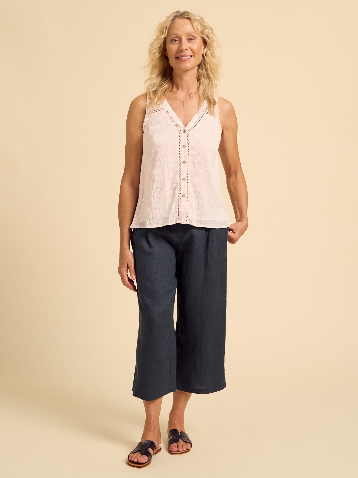 Woman wearing a light-colored sleeveless top and dark pants on a beige background