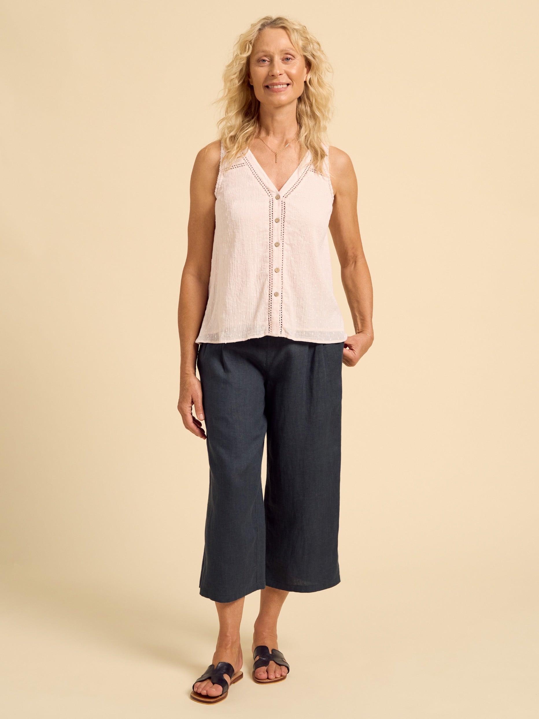 Woman wearing a light-colored sleeveless top and dark pants on a beige background