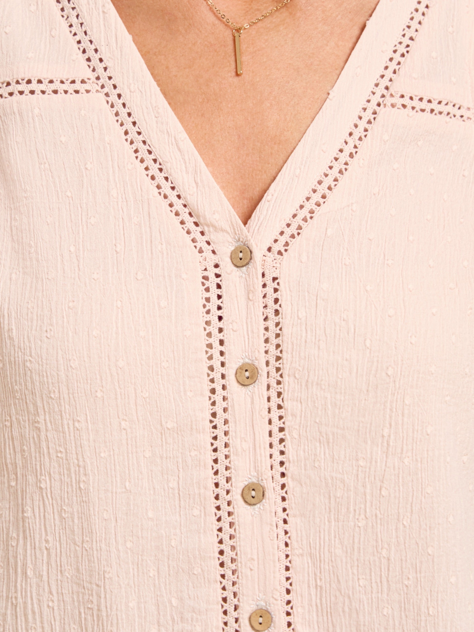 Close-up of a light pink blouse with button details and embroidery.