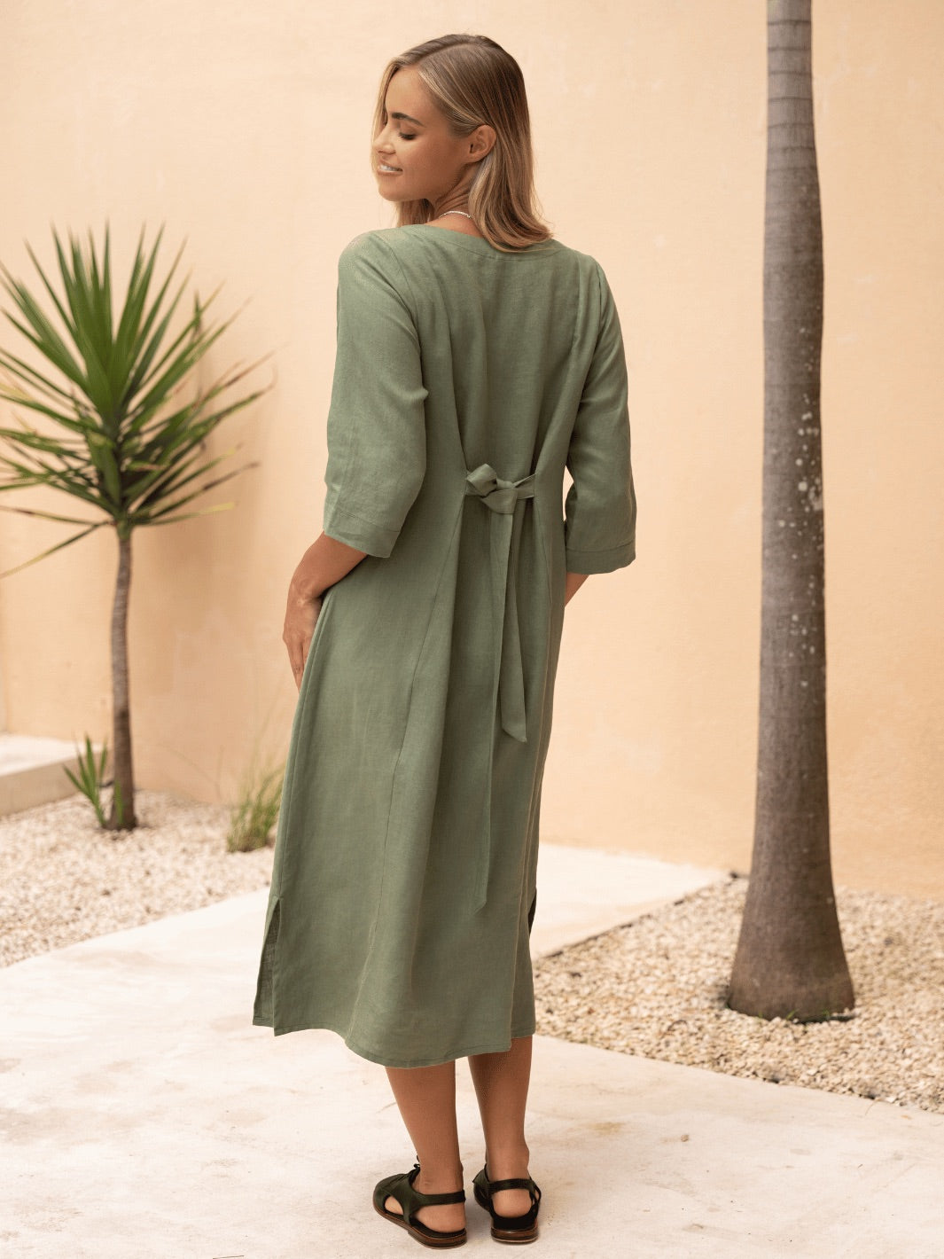 Woman wearing a green dress standing in a desert-like setting with palm trees.
