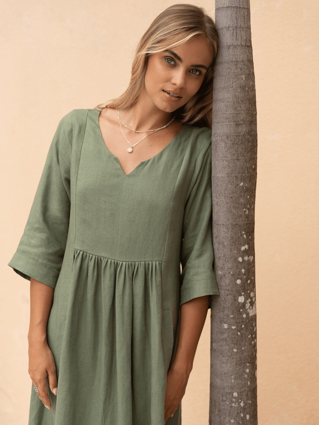 Woman in a green dress leaning against a palm tree