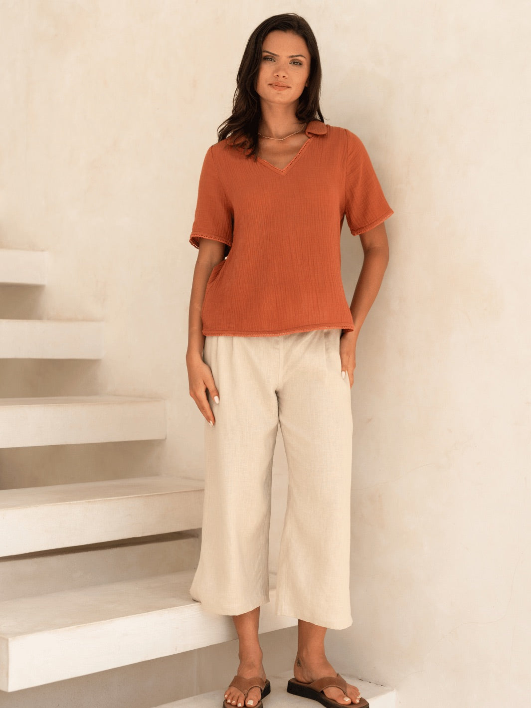 Woman wearing an orange top and beige pants standing on a staircase.