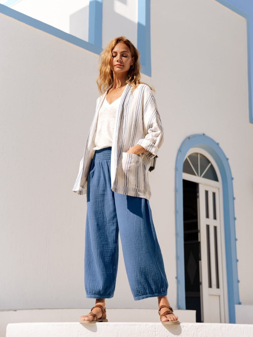Woman in a striped jacket and blue pants standing in front of a white building with blue accents.