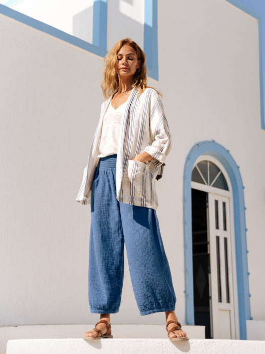 Woman in a striped jacket and blue pants standing in front of a white building with blue accents.