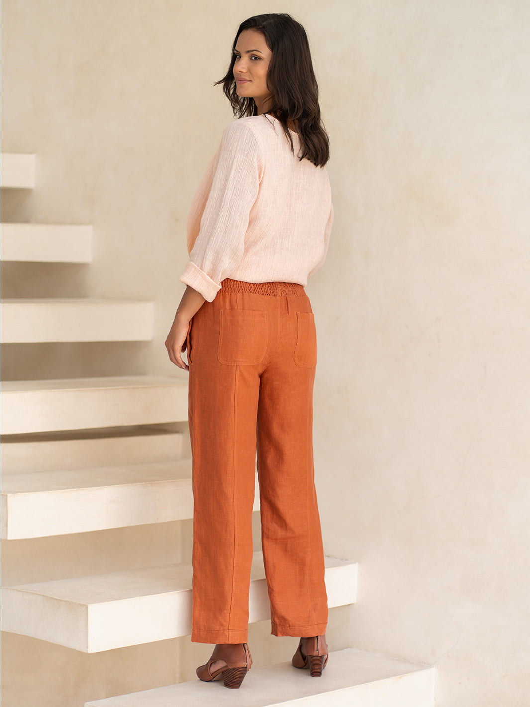 Woman wearing a light pink blouse and orange pants standing on a staircase.