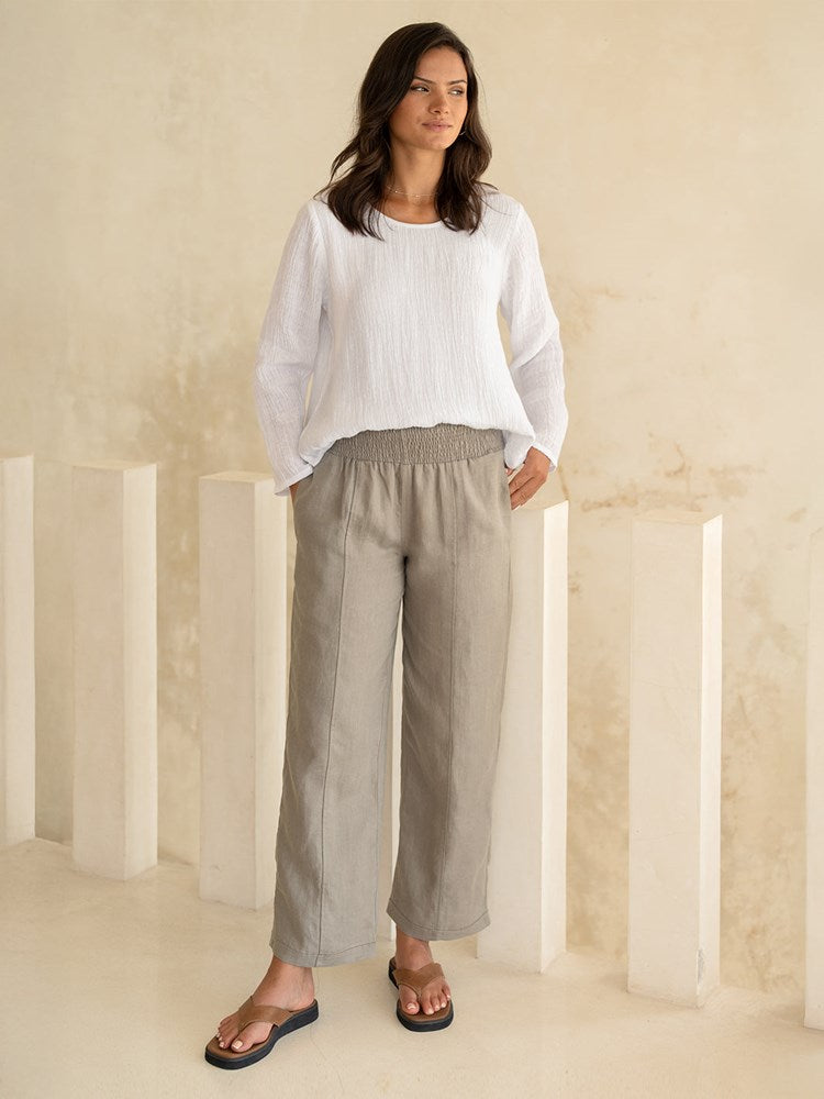 Woman wearing a white top and beige pants in a minimalistic setting