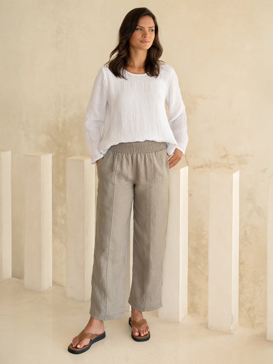 Woman wearing a white top and beige pants in a minimalistic setting