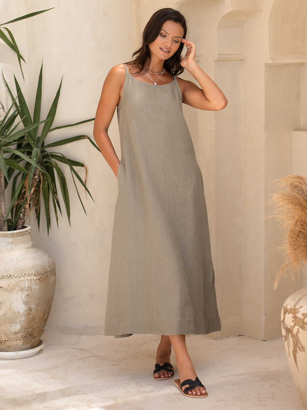 Woman wearing a sleeveless, knee-length dress in a neutral setting with decorative elements.