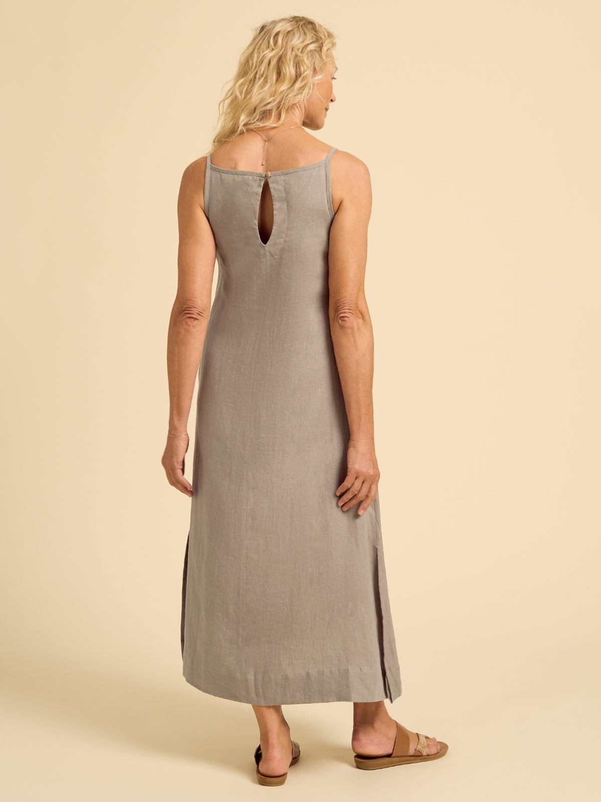 Woman wearing a beige sleeveless dress with a cutout back on a beige background