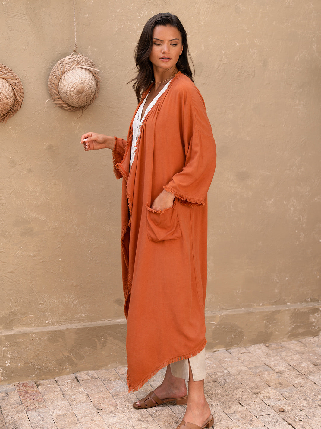 Woman wearing an orange long garment against a beige wall.