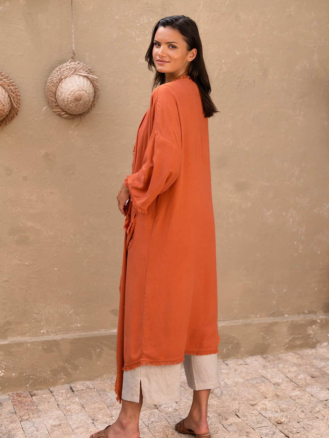 Woman wearing an orange long dress standing against a beige wall.